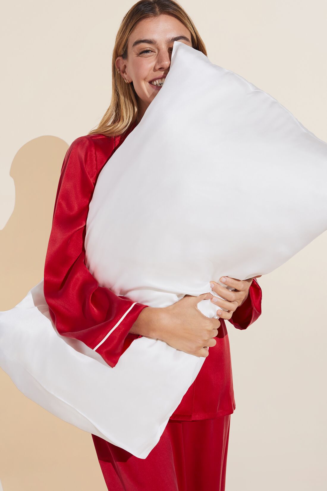 Model in a red washable silk PJ set holding a silk pillowcase