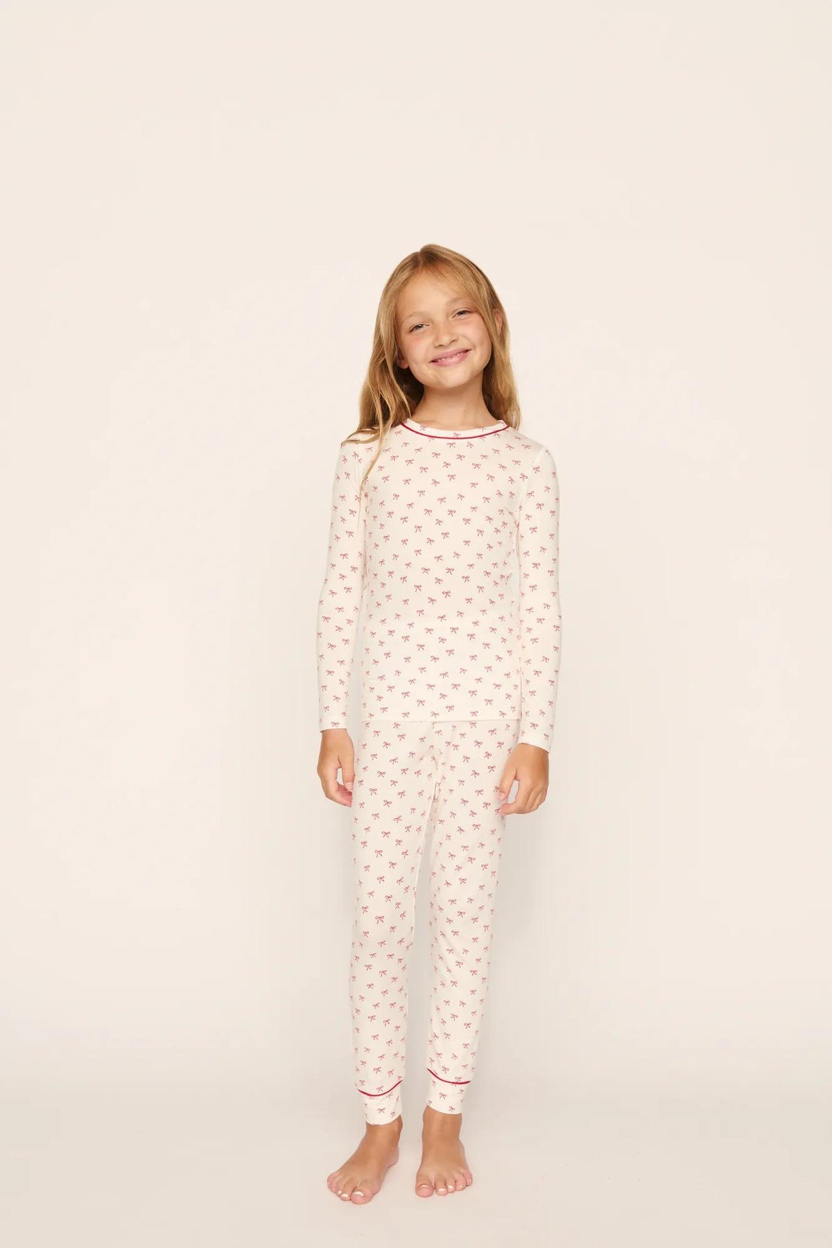 Model is wearing Kids Printed TENCEL™ Modal Unisex Long PJ Set in Mini Bow Ivory/Holly Red