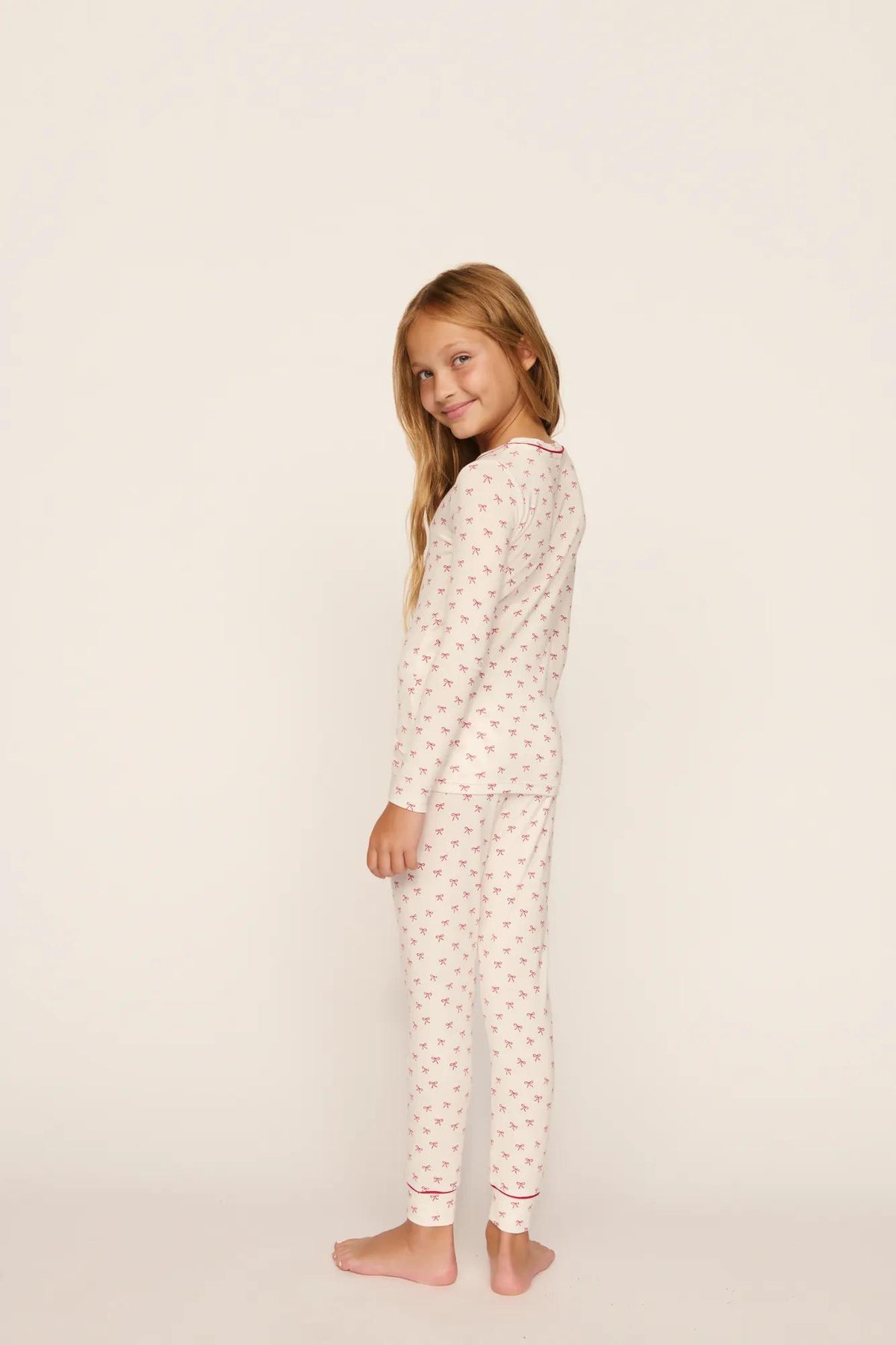 Model is wearing Kids Printed TENCEL™ Modal Unisex Long PJ Set in Mini Bow Ivory/Holly Red